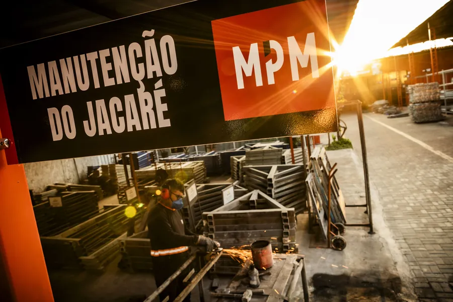 Setor de manutenção do Jacaré no pátio da MPM, com placa de identificação e técnico esmerilhando um perfil.