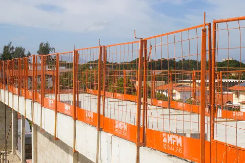 Guarda-corpo Jacaré com grade laranja fechando toda a periferia da laje de um prédio em construção.