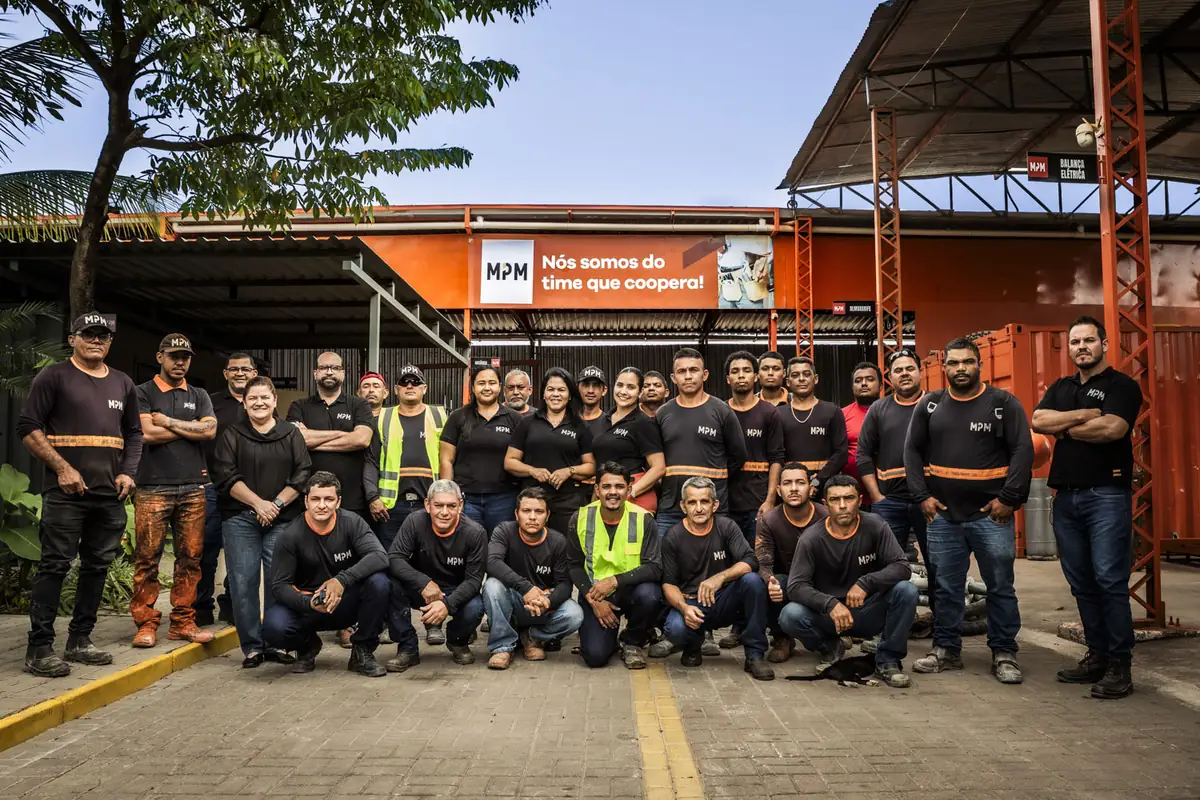 Equipe da MPM Locações reunida no pátio da sede, sob o painel da empresa.